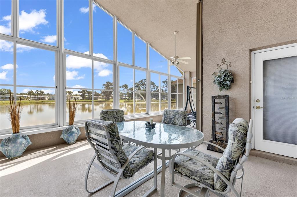 A sunroom with a glass-topped dining set overlooks a lake through large, multi-pane windows — 24308 BUCKINGHAM WAY, PUNTA GORDA, FL