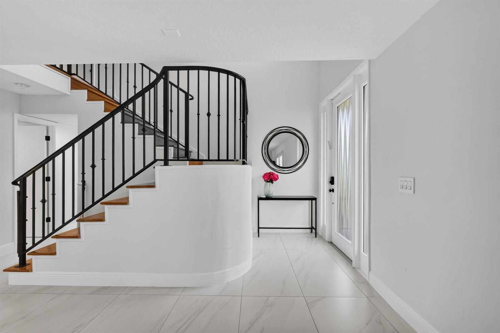 A bright entryway features white tile floors, a curved staircase with black railings, and a console — 6188 Celadon Circle, Palm Beach Gardens FL 33418, PALM BEACH GARDENS, FL