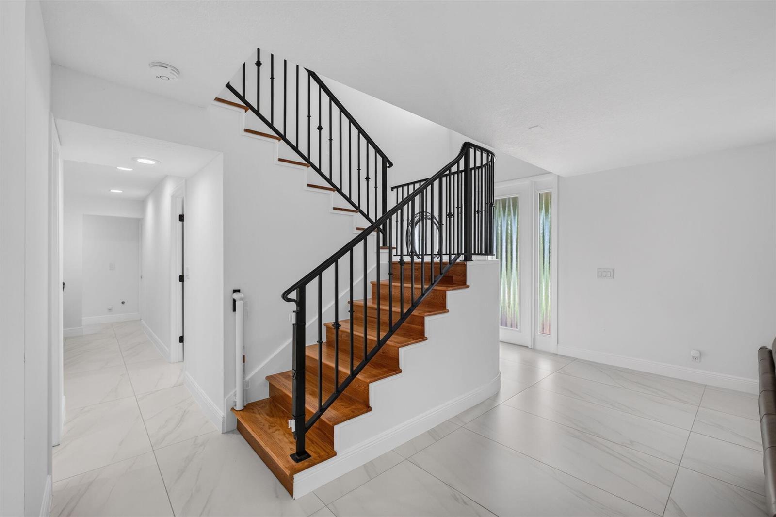 A staircase with wooden treads and black metal railings sits in a white-walled entryway — 6188 Celadon Circle, Palm Beach Gardens FL 33418, PALM BEACH GARDENS, FL