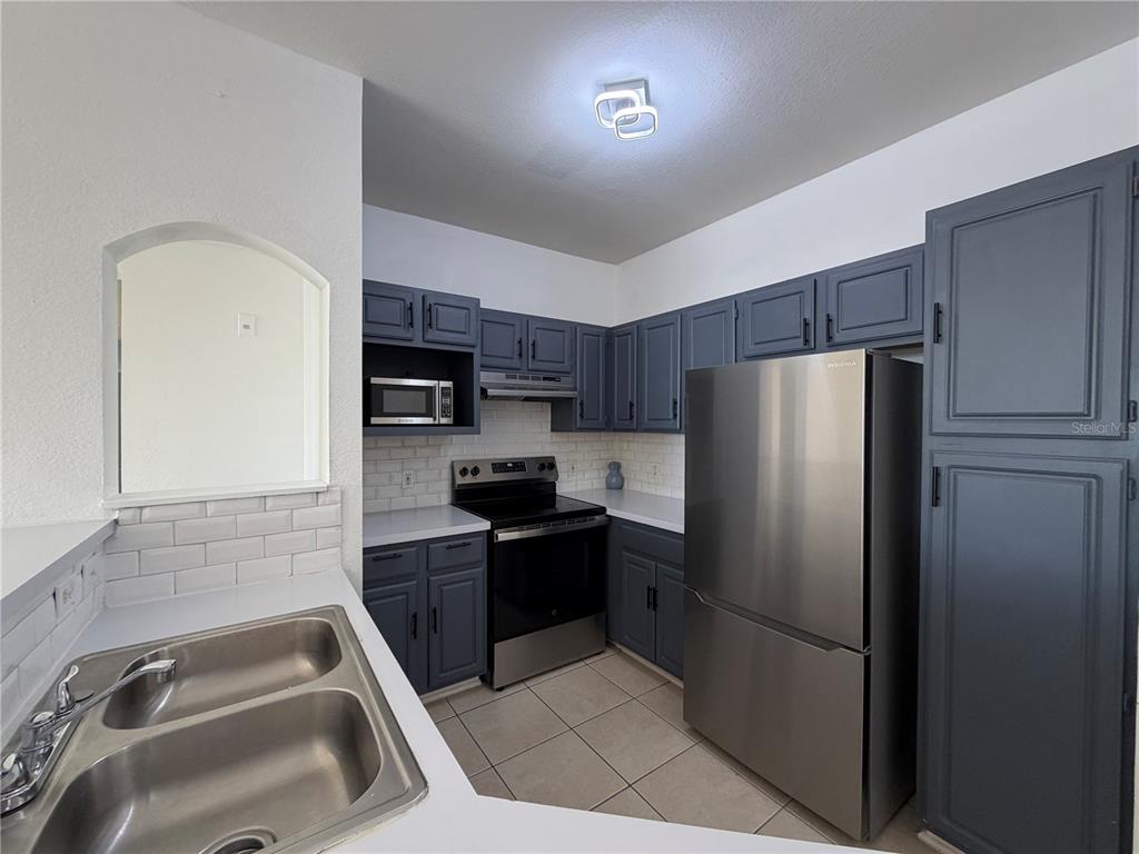 A kitchen features dark blue cabinets, stainless steel appliances, white countertops, and a double sink — 3315 PARKCHESTER SQUARE BOULEVARD UNIT 301, ORLANDO, FL