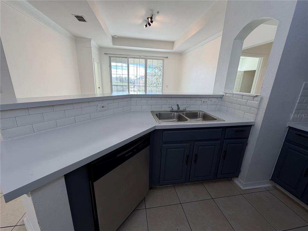 A kitchen features blue cabinets, white countertops, a subway tile backsplash, and a double sink — 3315 PARKCHESTER SQUARE BOULEVARD UNIT 301, ORLANDO, FL