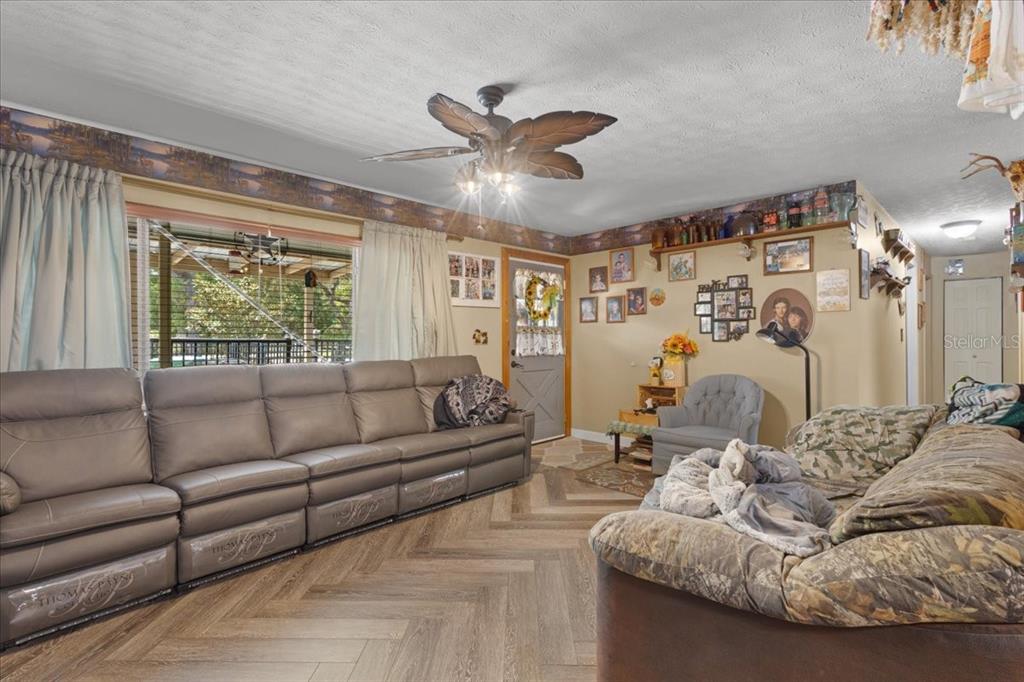 A living room features a large leather sofa, herringbone flooring, and a ceiling fan — 8731 NW 127TH PLACE, CHIEFLAND, FL