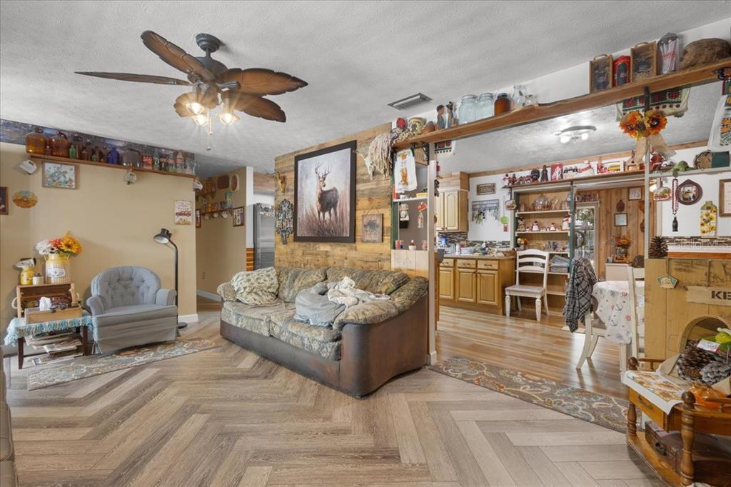 A living room with wood-plank accent walls, herringbone flooring, and an open view to the kitchen — 8731 NW 127TH PLACE, CHIEFLAND, FL