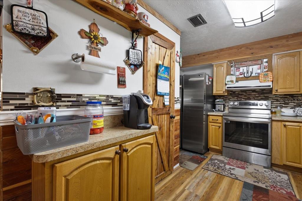 A kitchen with wood cabinets, stainless steel appliances, a tile backsplash, and a wooden door — 8731 NW 127TH PLACE, CHIEFLAND, FL