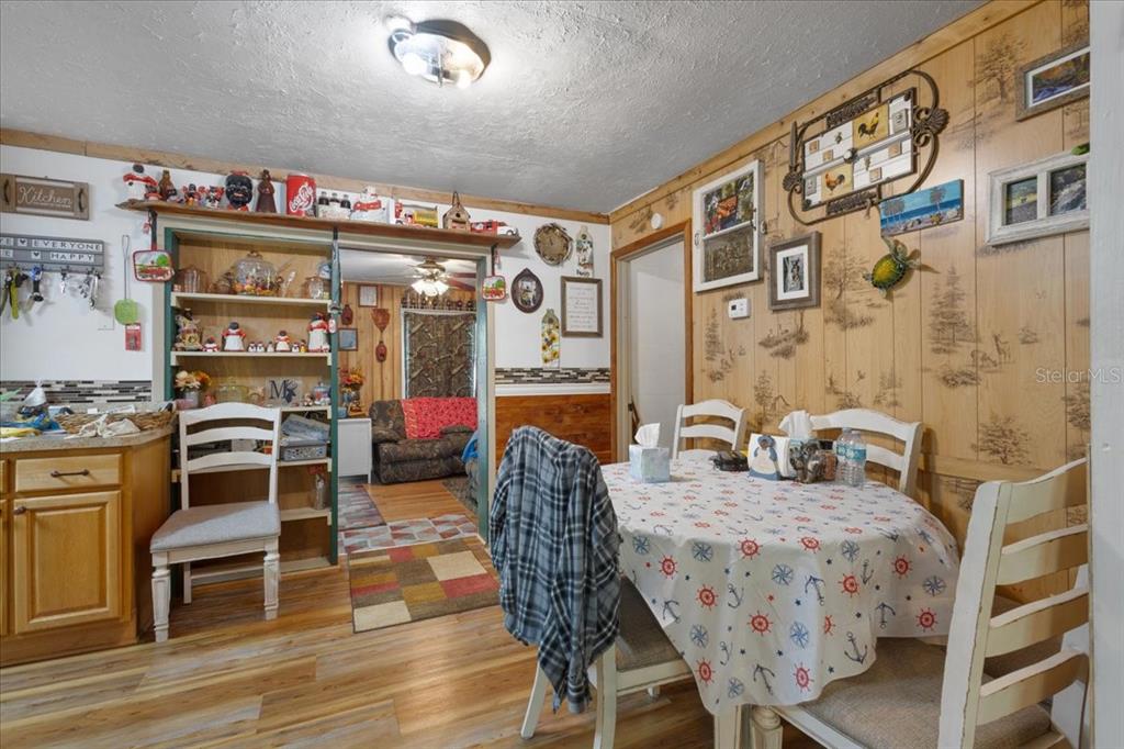 A dining area features wood-paneled walls, a round table with chairs, and an adjacent kitchen — 8731 NW 127TH PLACE, CHIEFLAND, FL