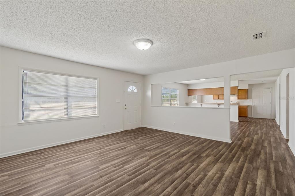 An empty living room features wood-look flooring, white walls, and a pass-through to the kitchen — 6711 INTERBAY BOULEVARD, TAMPA, FL