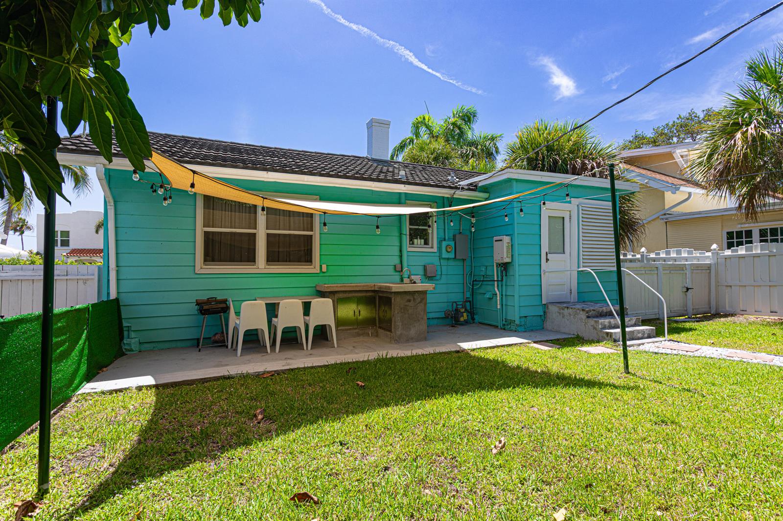 The backyard of a teal house features a concrete patio, outdoor kitchen, and shade sail — 305 N Lakeside Drive, FL 33460, FL
