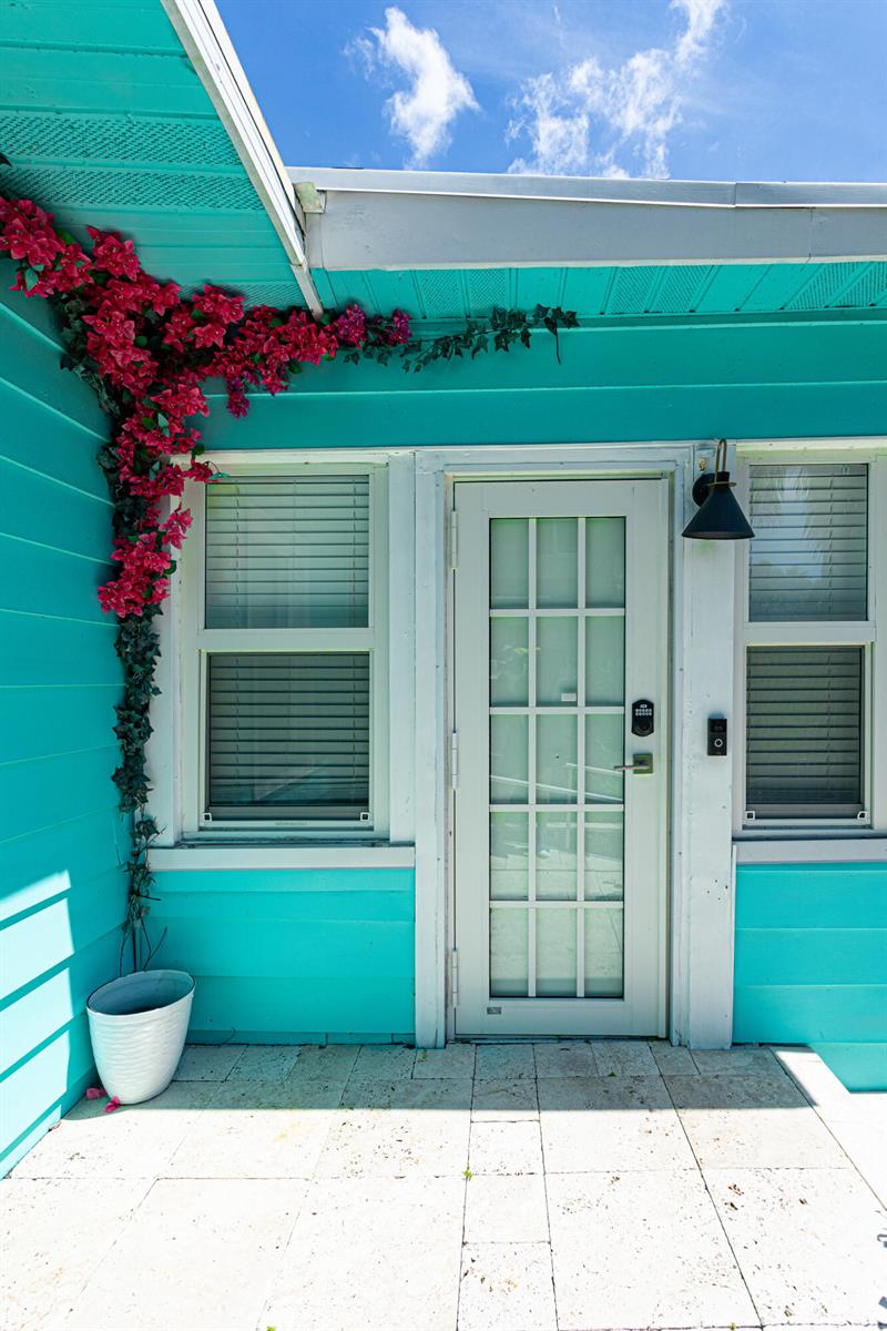 A turquoise house exterior features a white front door, windows with blinds, and climbing bougainvillea — 305 N Lakeside Drive, FL 33460, FL