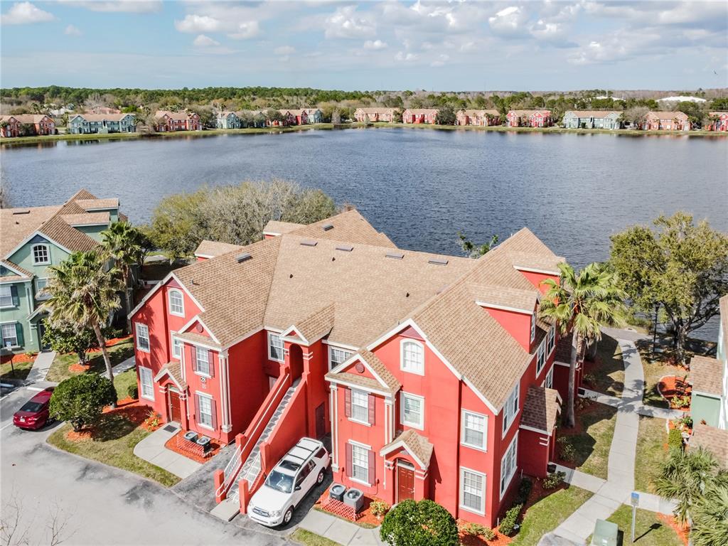 An aerial view shows a red multi-story apartment building situated next to a large lake — 9632 LAKE CHASE ISLAND WAY UNIT 9632, TAMPA, FL