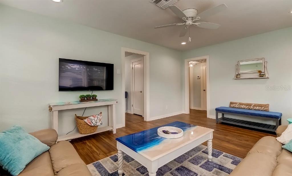 A living room features light blue walls, wood-look flooring, a ceiling fan, and coastal decor — 1226 SEDEEVA CIRCLE S, CLEARWATER, FL