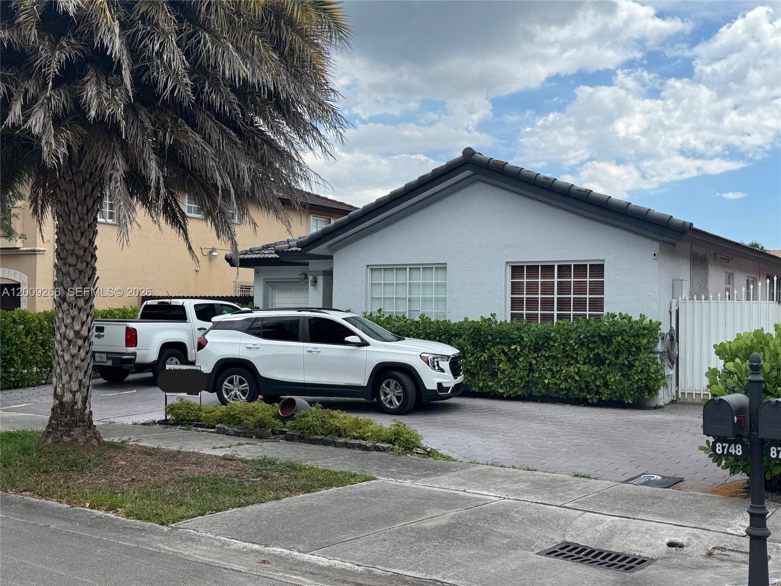 A white single-story house with a paved driveway, two parked vehicles, and a palm tree — 8748 NW 143rd Ter, Miami Lakes FL 33018, MIAMI LAKES, FL