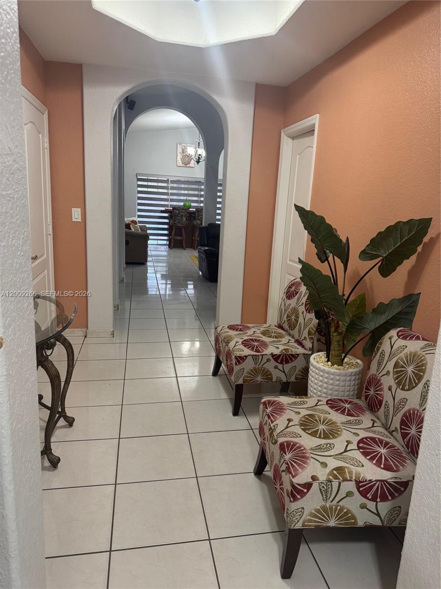 A tiled hallway features an arched entryway, peach-colored walls, and two patterned accent chairs — 8748 NW 143rd Ter, Miami Lakes FL 33018, MIAMI LAKES, FL