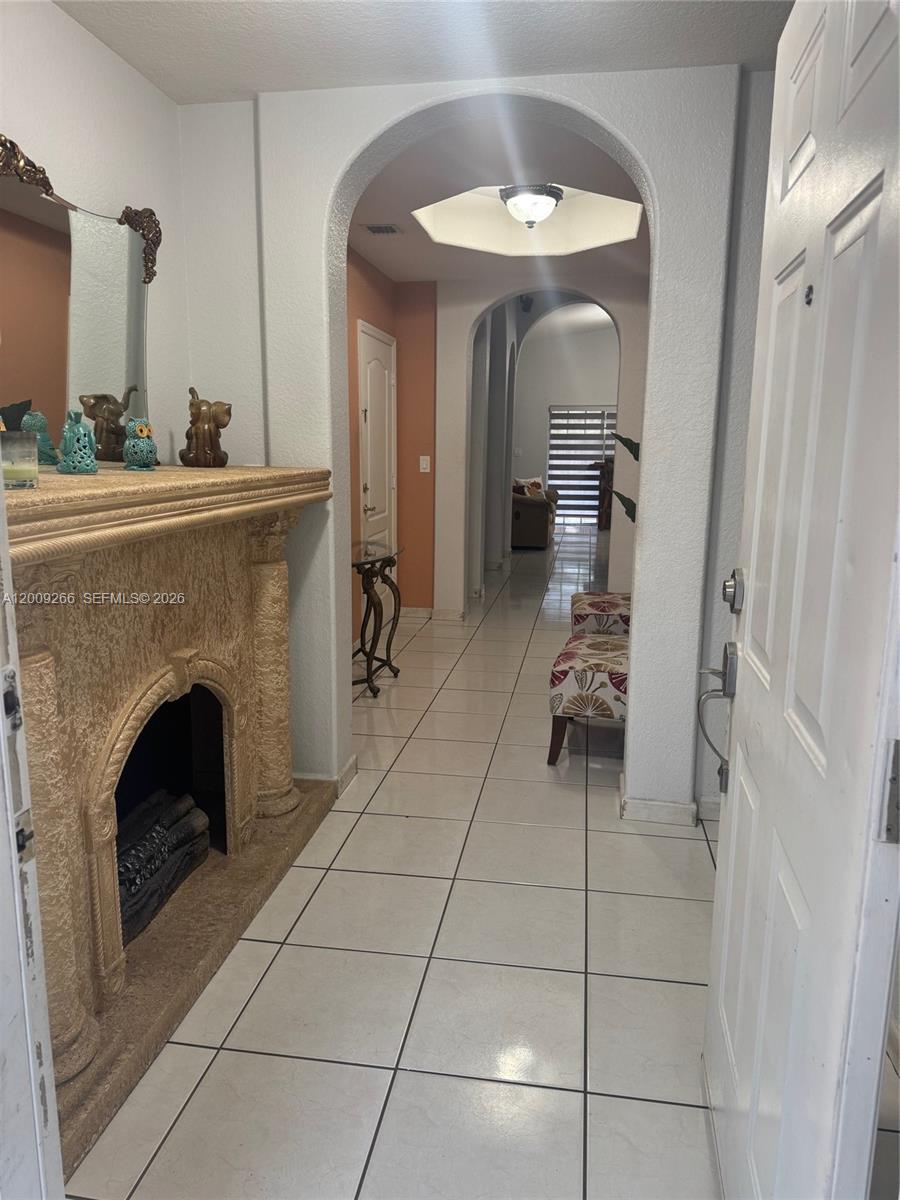 An entryway features a textured fireplace, tiled floors, and an arched hallway leading inside — 8748 NW 143rd Ter, Miami Lakes FL 33018, MIAMI LAKES, FL