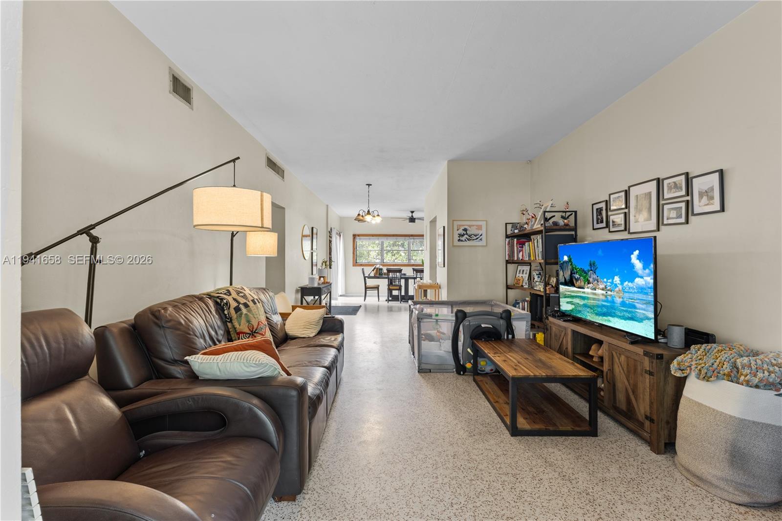 A living room with a brown leather sofa, television, and dining area in the background — 325 Bird Rd, Coral Gables FL 33146, CORAL GABLES, FL