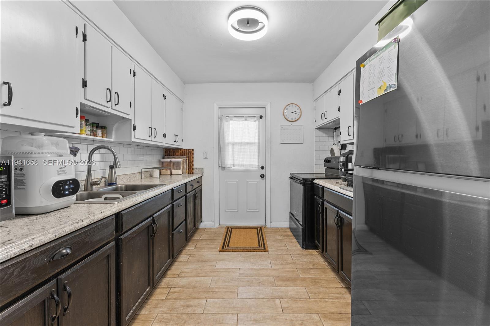 A galley kitchen features white upper cabinets, dark lower cabinets, stainless steel appliances, and tile flooring — 325 Bird Rd, Coral Gables FL 33146, CORAL GABLES, FL