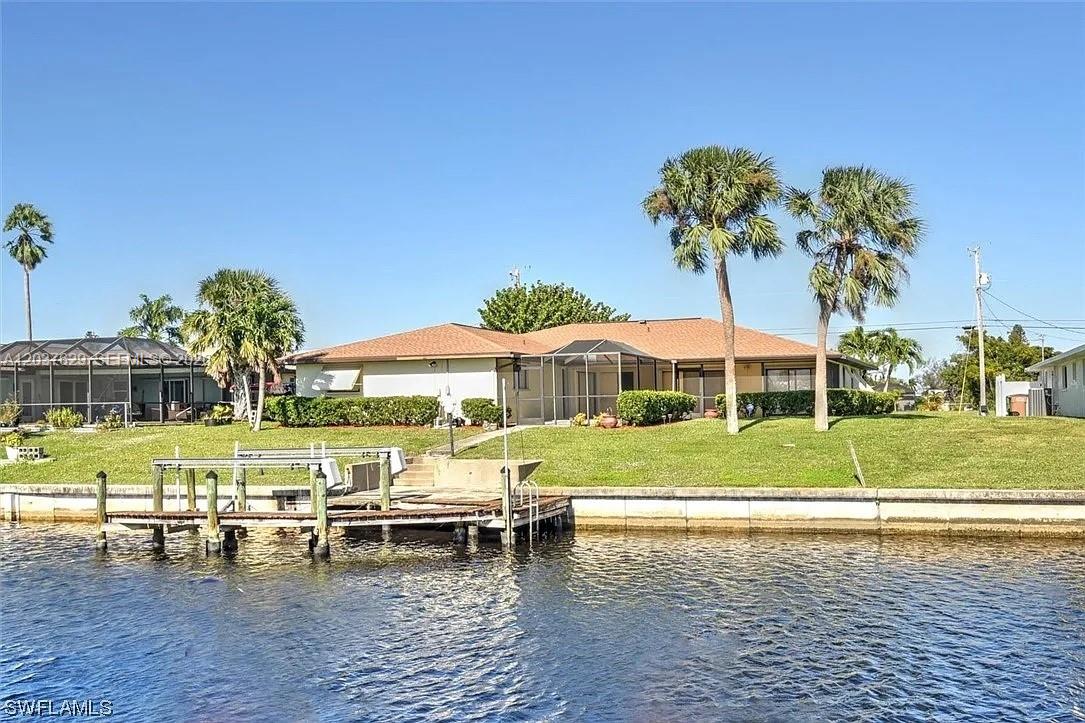 A single-story house with a screened lanai sits on a grassy lot beside a canal — 1822 SE 11 Ter, Cape Coral FL 33990, CAPE CORAL, FL
