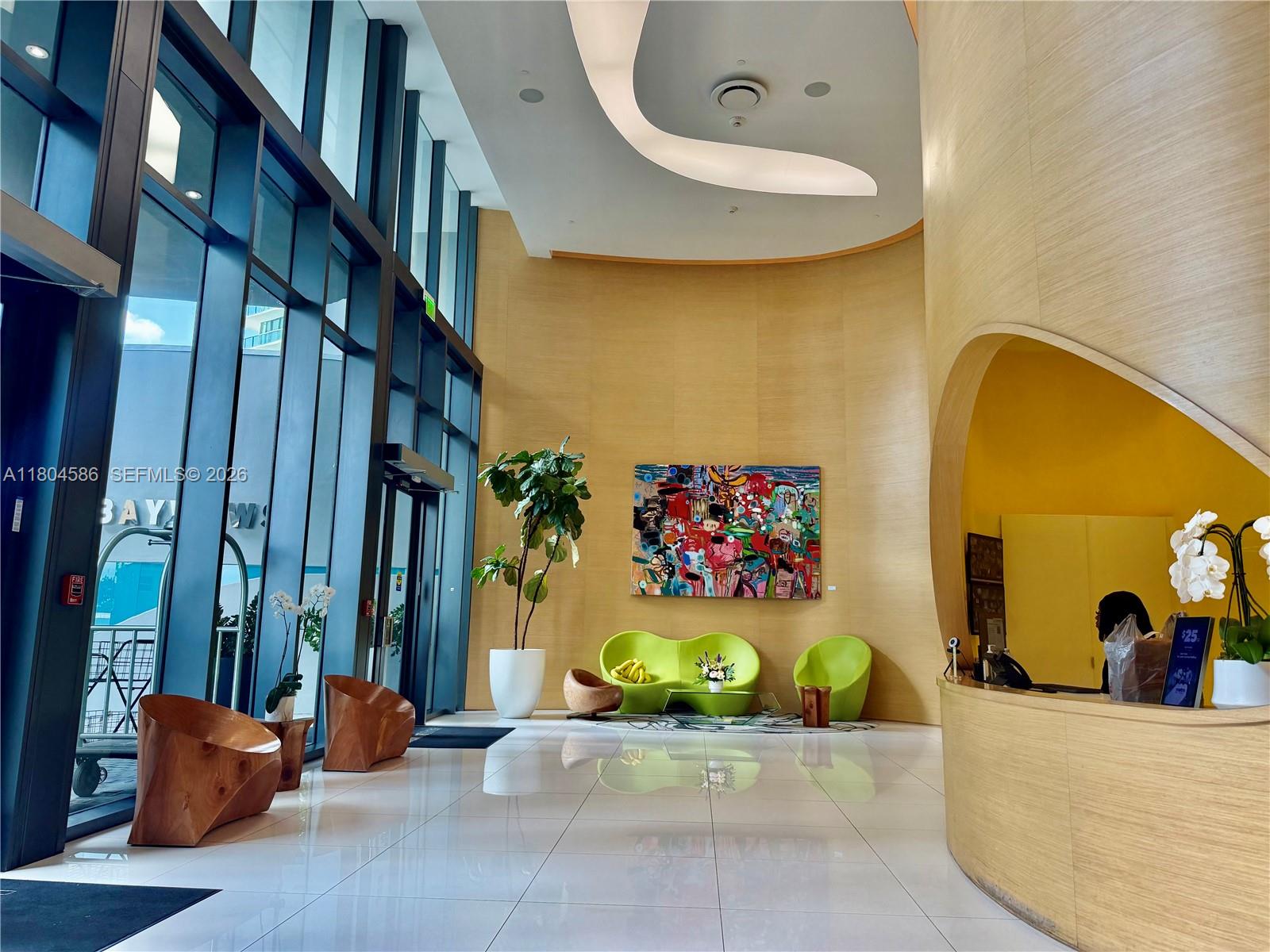 A modern building lobby features a curved wood-paneled wall, floor-to-ceiling windows, and contemporary furniture — 501 NE 31st St # 2903, Miami FL 33137, MIAMI, FL