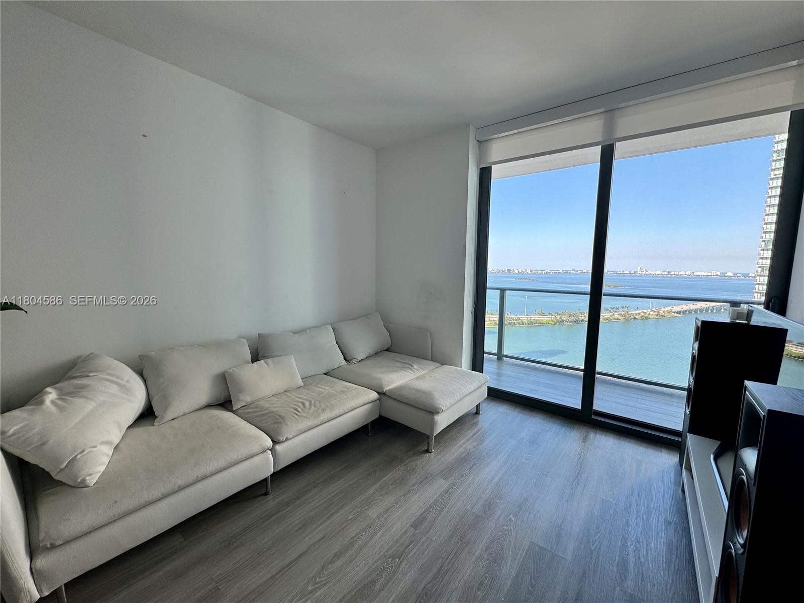 A living room features a white sectional sofa, wood-look flooring, and floor-to-ceiling windows overlooking water — 501 NE 31st St # 2903, Miami FL 33137, MIAMI, FL