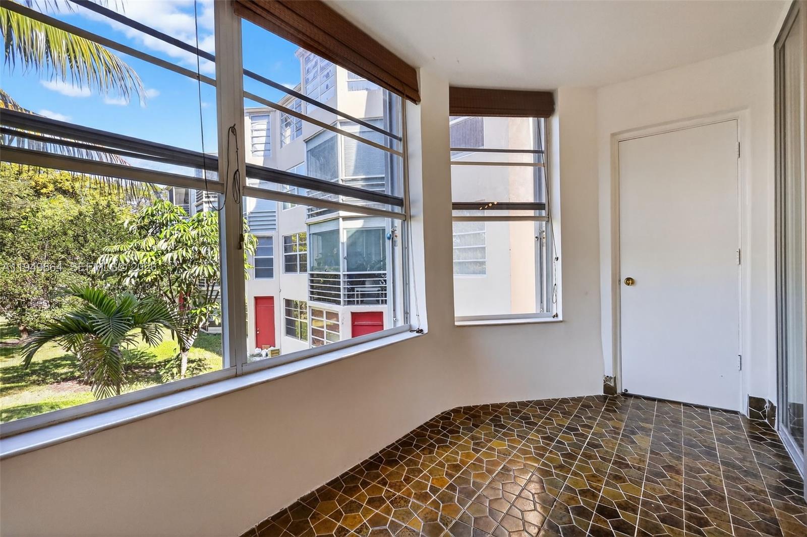 A sunroom with patterned tile flooring, large windows, and a white door — 1501 NE 191st St # C212, Miami FL 33179, MIAMI, FL
