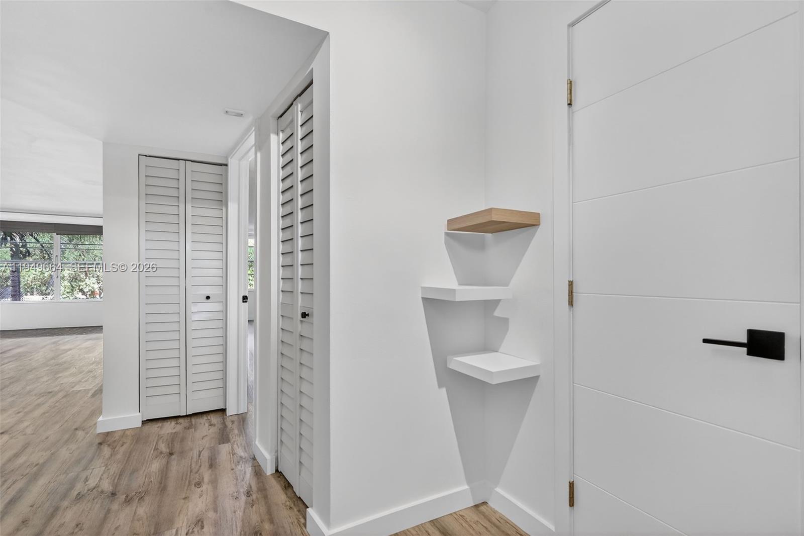 A hallway features white louvered closet doors, wood-look flooring, and three small corner wall shelves — 1501 NE 191st St # C212, Miami FL 33179, MIAMI, FL