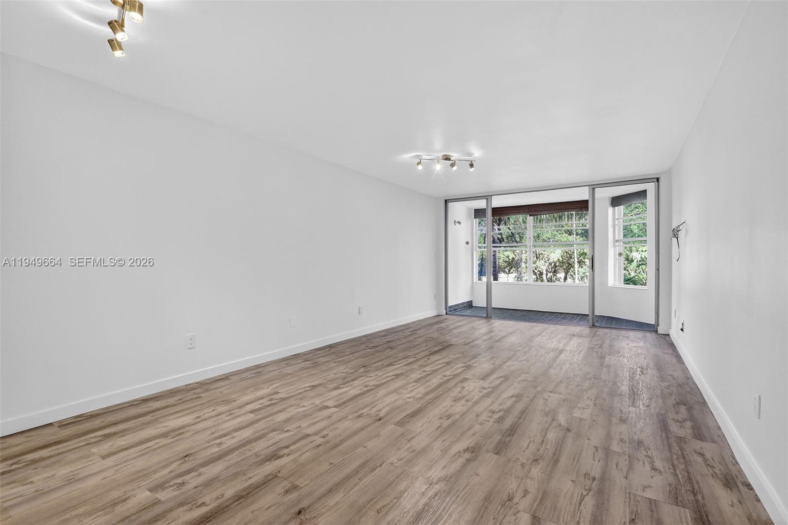 An empty room features light wood-look flooring, white walls, and a sliding glass door — 1501 NE 191st St # C212, Miami FL 33179, MIAMI, FL