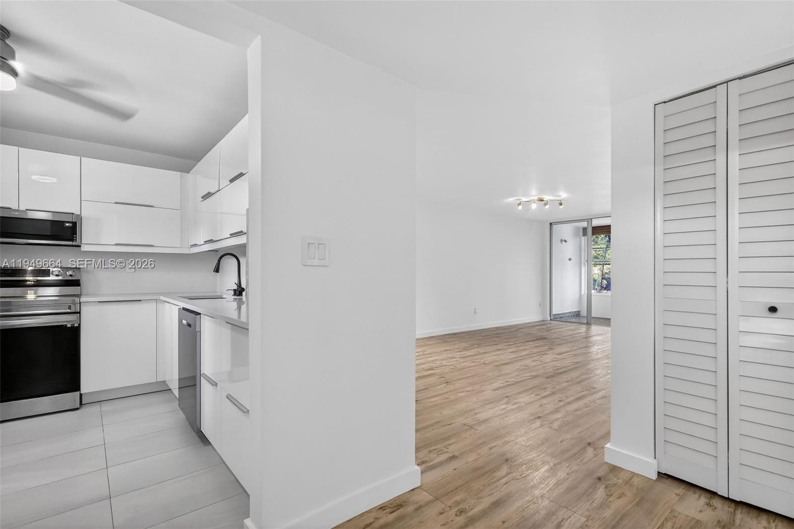 A white kitchen with stainless steel appliances opens into a living area with wood flooring — 1501 NE 191st St # C212, Miami FL 33179, MIAMI, FL