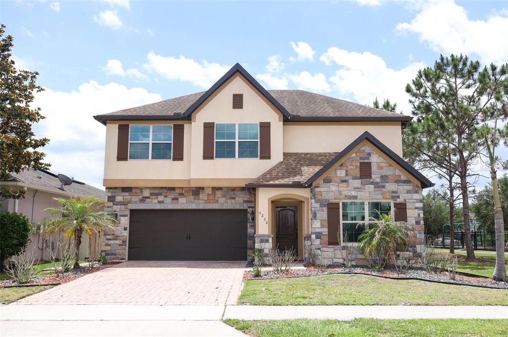A two-story house with a stone facade, brown garage door, and a brick driveway — 5232 VILLA ROSA AVENUE, ST CLOUD, FL