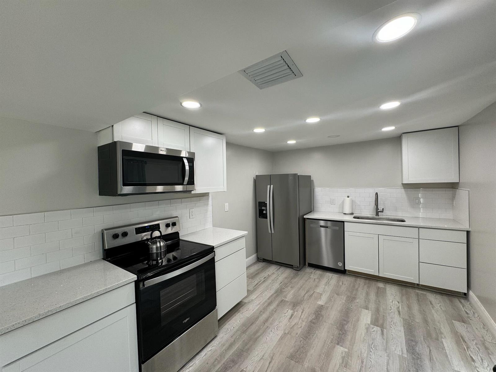 A modern kitchen features white cabinets, stainless steel appliances, subway tile backsplash, and light flooring — 4679 SE Ebbtide Avenue # O, Stuart FL 34997, STUART, FL