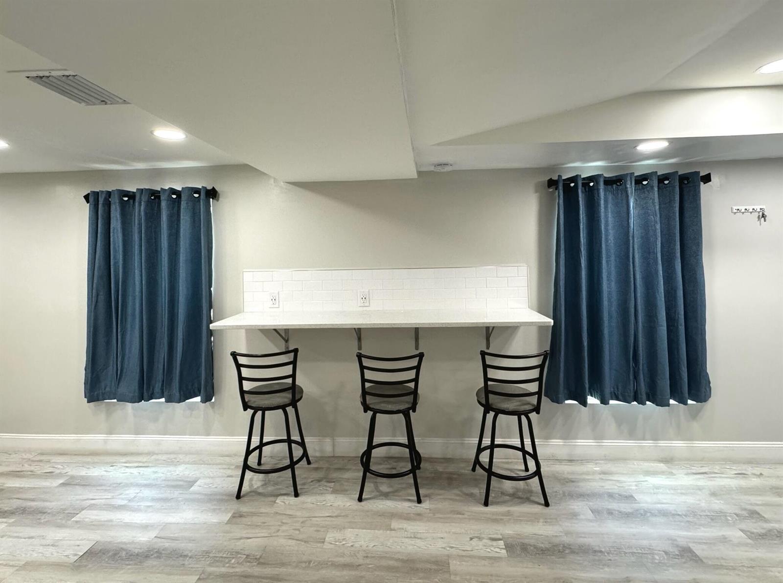 A basement room features a white countertop bar with three stools and blue curtains — 4679 SE Ebbtide Avenue # O, Stuart FL 34997, STUART, FL