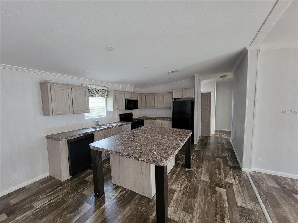 A kitchen features light wood cabinets, a dark island, and dark laminate countertops — 16625 SE 102ND AVENUE ROAD, SUMMERFIELD, FL