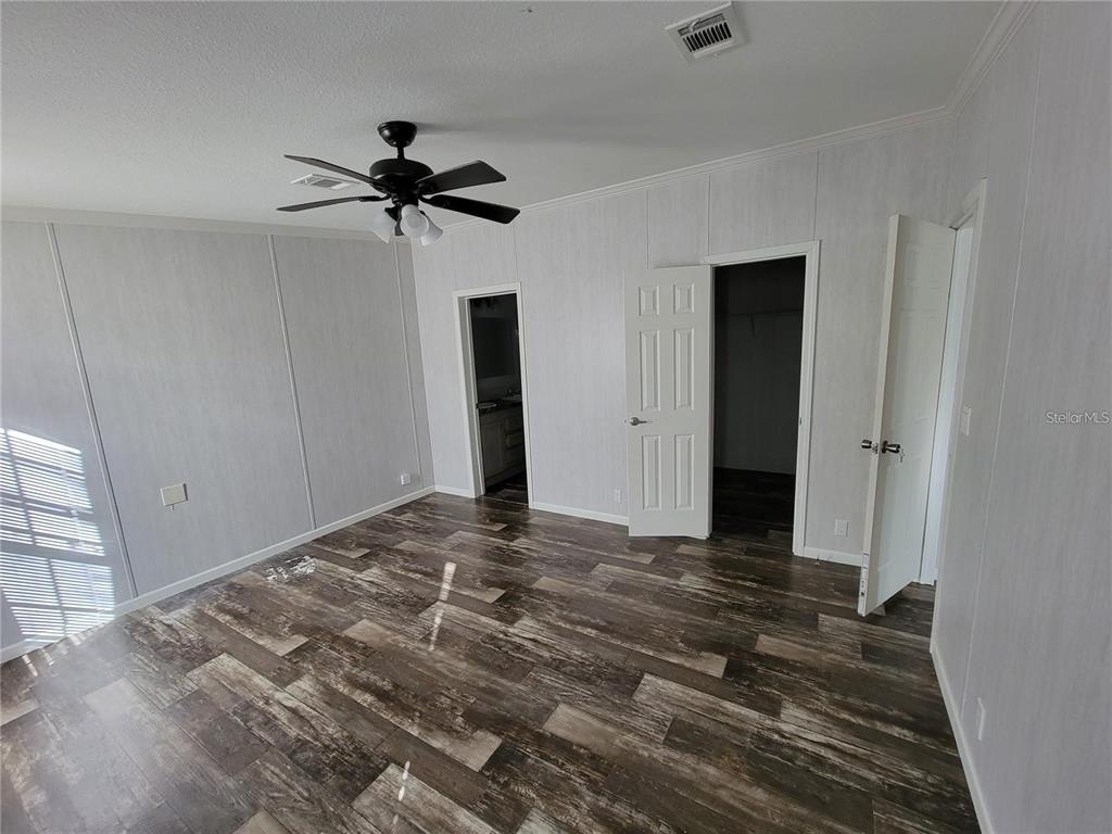 A bedroom features wood-look flooring, white paneled walls, a ceiling fan, and two doorways — 16625 SE 102ND AVENUE ROAD, SUMMERFIELD, FL