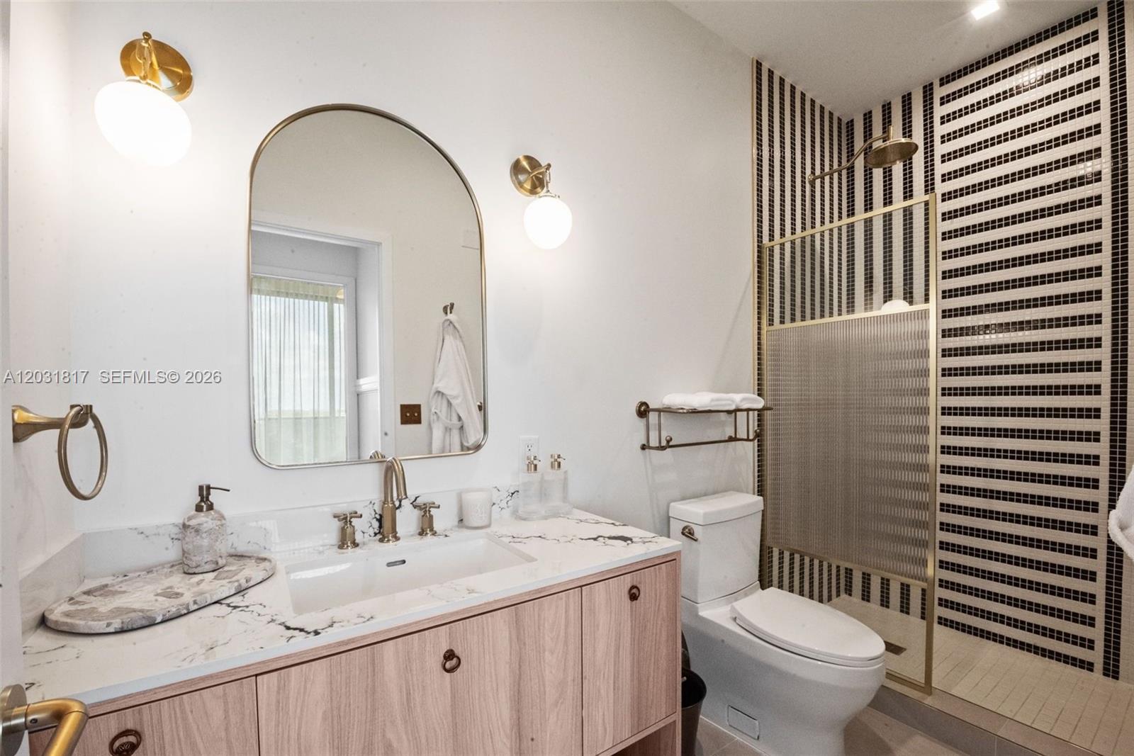 A bathroom features a wood vanity, arched mirror, and a shower with striped tile walls — 2700 NW 2ND AVE # 417, Miami FL 33127, MIAMI, FL