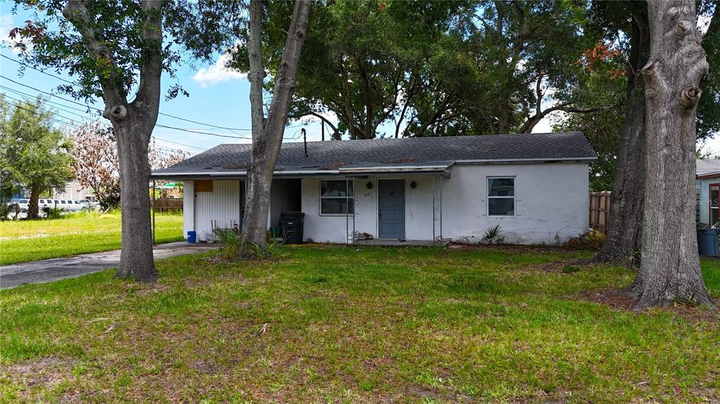 A single-story white house with a covered entryway stands behind large trees on a lawn — 721 S WOODLAND STREET, WINTER GARDEN, FL