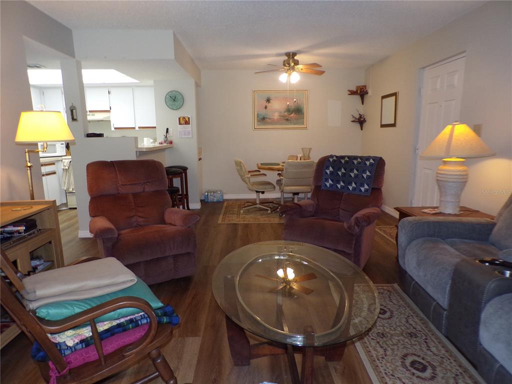 A living room and dining area feature wood-look flooring, a glass coffee table, and recliners — 19505 QUESADA AVENUE UNIT C207, PORT CHARLOTTE, FL