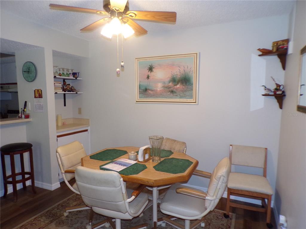 A dining room features an octagonal wooden table, four chairs, a ceiling fan, and artwork — 19505 QUESADA AVENUE UNIT C207, PORT CHARLOTTE, FL