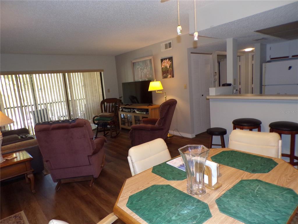 A dining area with a wooden table overlooks a living room with a television — 19505 QUESADA AVENUE UNIT C207, PORT CHARLOTTE, FL