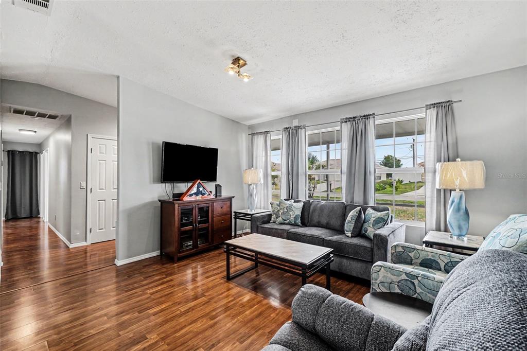 A living room features wood flooring, a grey sofa, a television, and large windows — 316 SW 19TH TERRACE, CAPE CORAL, FL