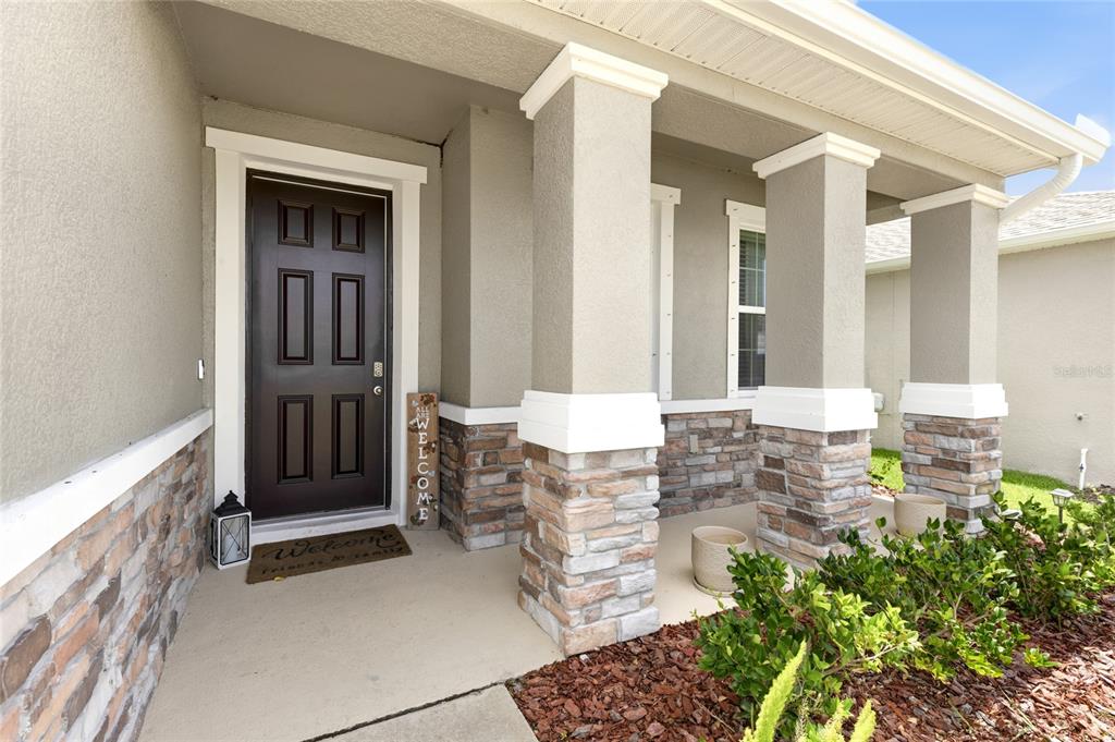 A covered front porch features a dark brown door, stone accents, and three square columns — 5603 NIGHT OWL TERRACE, PALMETTO, FL
