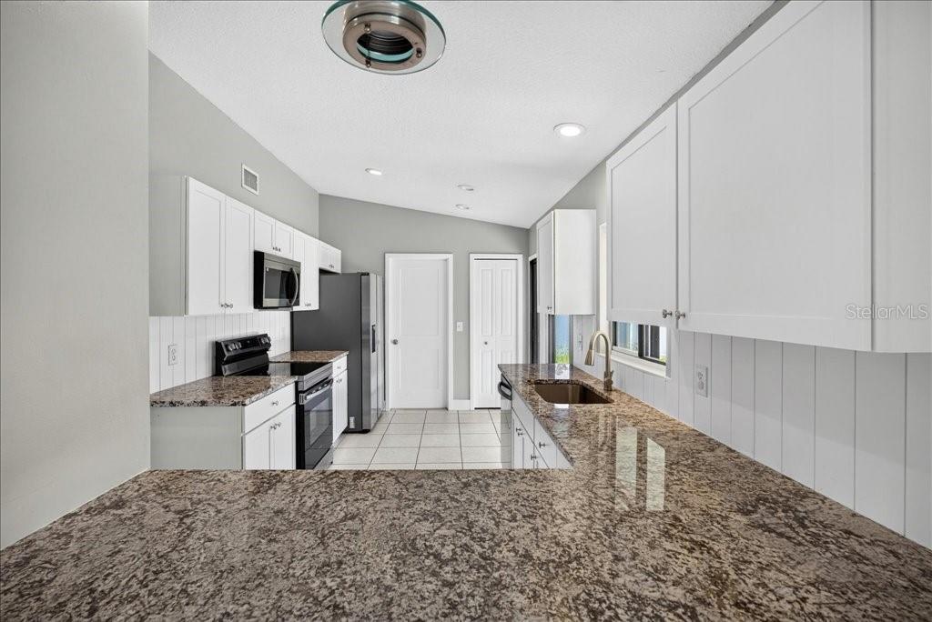 A kitchen features white cabinets, granite countertops, a stainless steel stove, and tiled flooring — 40 BOULDER ROCK DRIVE, PALM COAST, FL