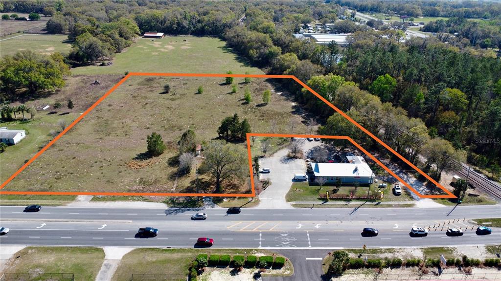 An aerial view shows a large, vacant lot adjacent to a commercial building and road — 6910 SE HIGHWAY 42, SUMMERFIELD, FL