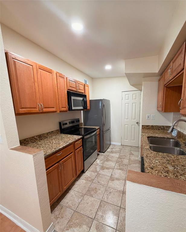 A kitchen features wood cabinets, granite countertops, stainless steel appliances, and tile flooring — 1503 W LINEBAUGH AVENUE, TAMPA, FL