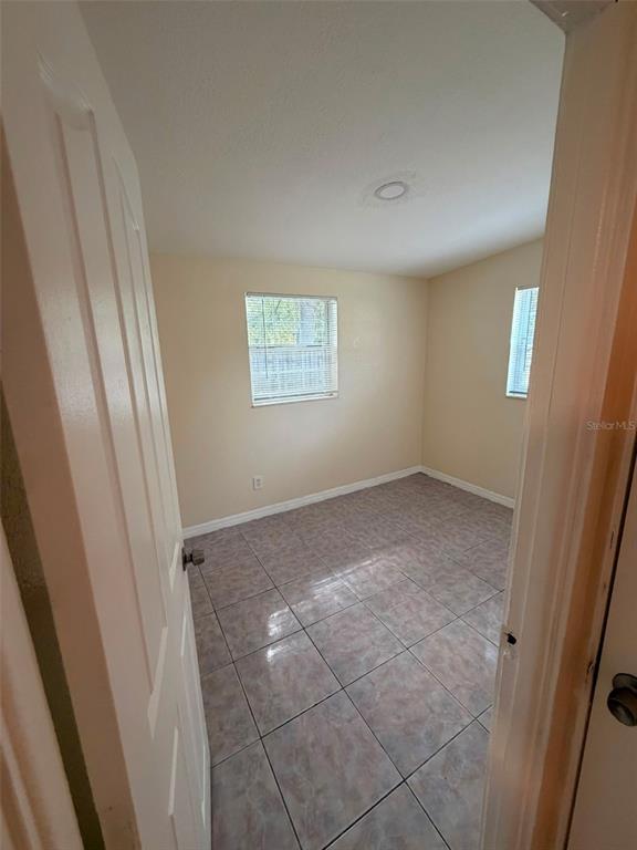An empty bedroom features light-colored walls, tiled flooring, and two windows — 1503 W LINEBAUGH AVENUE, TAMPA, FL