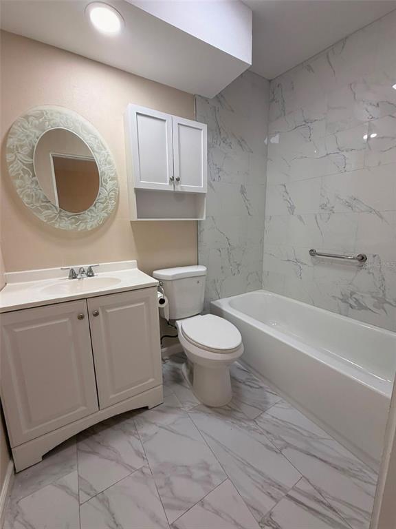 A bathroom features a white vanity, a toilet, and a bathtub with marble-patterned tile walls — 1503 W LINEBAUGH AVENUE, TAMPA, FL