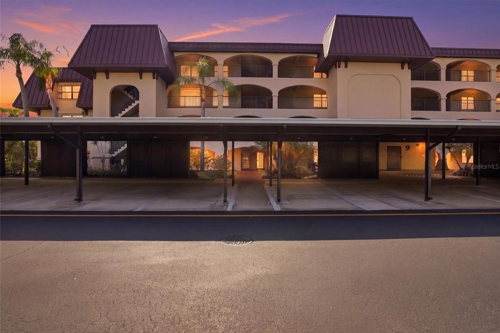 A multi-story apartment building with a covered parking structure in the foreground at sunset — 23465 HARBORVIEW ROAD UNIT 913, PUNTA GORDA, FL