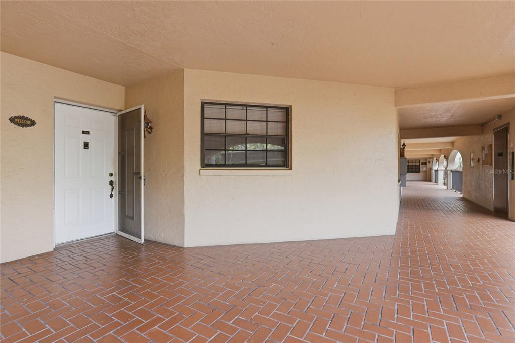 A covered outdoor walkway features a white front door and a window on a beige wall — 23465 HARBORVIEW ROAD UNIT 913, PUNTA GORDA, FL