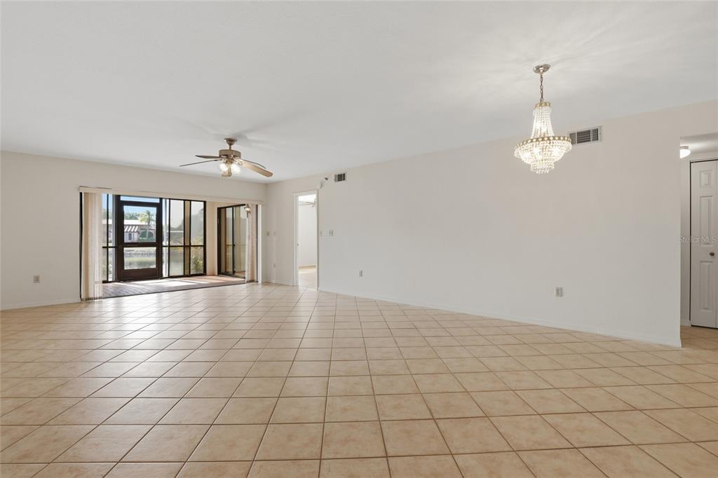 A spacious, tiled living room features a ceiling fan, a crystal chandelier, and sliding doors — 23465 HARBORVIEW ROAD UNIT 913, PUNTA GORDA, FL