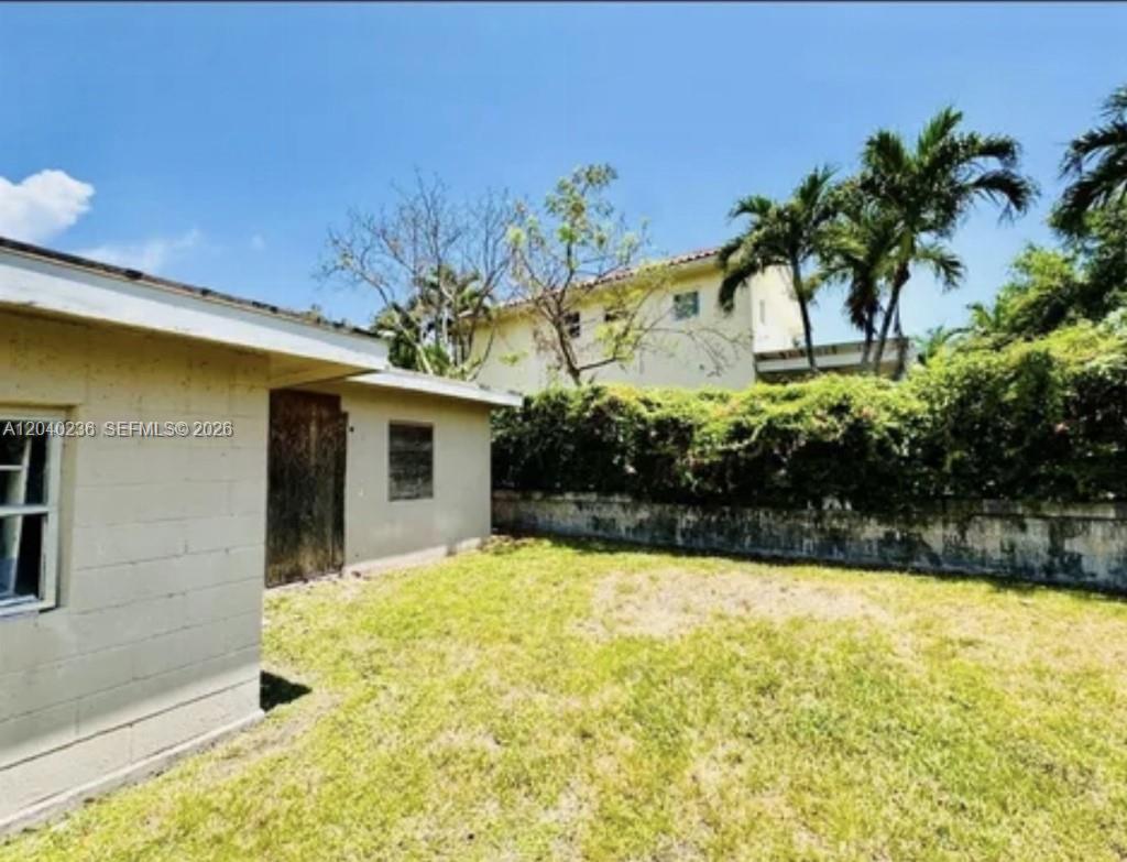 A grassy backyard features a light-colored exterior wall, a wooden door, and palm trees — 2616 NE 214th St, Miami FL 33180, MIAMI, FL