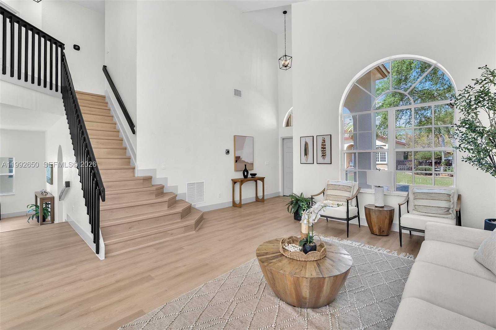A bright living room features a wooden staircase, light flooring, and a large arched window — 9732 NW 32nd St, Doral FL 33172, DORAL, FL