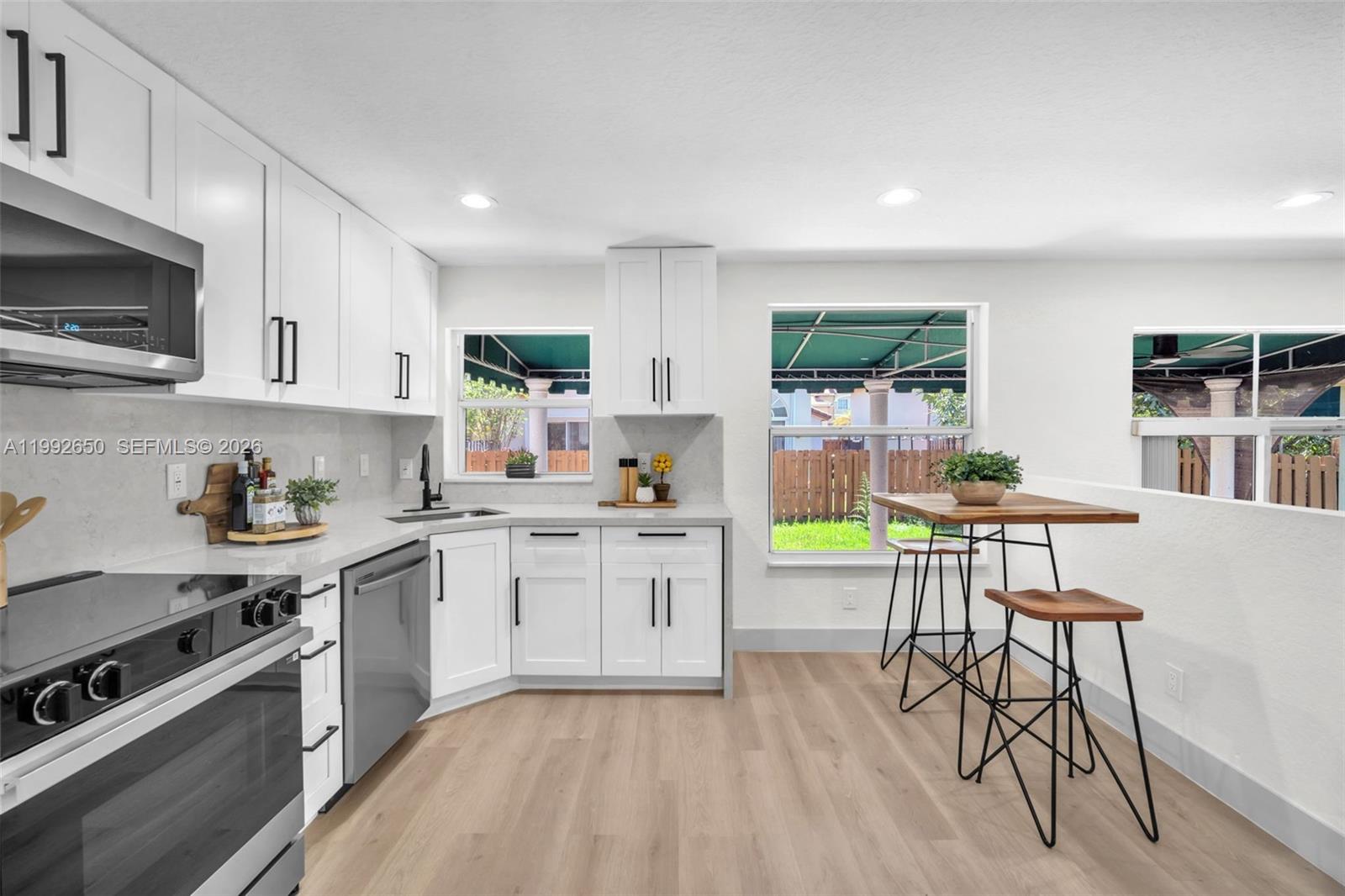 A bright kitchen features white cabinets, stainless steel appliances, light wood flooring, and a dining area — 9732 NW 32nd St, Doral FL 33172, DORAL, FL