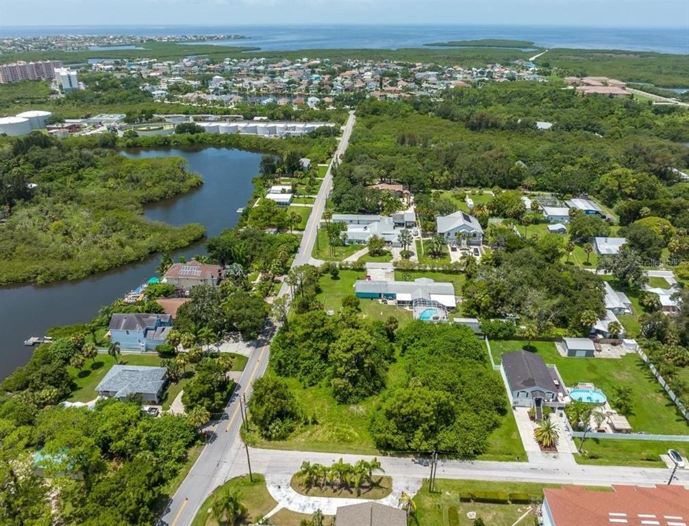 An aerial view shows a residential neighborhood with houses, lush trees, and a nearby waterway — 6307 OELSNER STREET UNIT 11&12, NEW PORT RICHEY, FL
